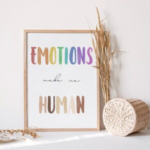 K&ouml;nnte beinhalten: Ein gerahmter Druck mit dem Text "EMOTIONS make us HUMAN" in Regenbogen- und braunen Aquarellbuchstaben. Der Druck ist auf wei&szlig;em Hintergrund und hat einen hellen Holzrahmen.