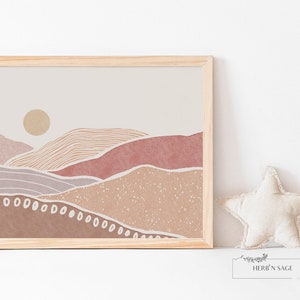 Peut inclure: Une impression encadr&eacute;e d'un paysage minimaliste avec un soleil, des collines et un fond textur&eacute; dans des tons de brun, rose et beige. L'impression est dans un cadre en bois clair.