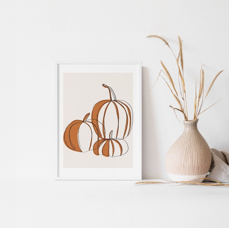 A seasonal fall print. This fall print has three pumpkins draw with a continuous black line. Random parts of the three pumpkins are painted orange and the background is a beige with a white border.