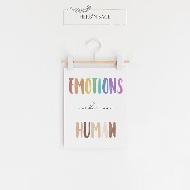 K&ouml;nnte beinhalten: Ein wei&szlig;er Poster mit dem Text "EMOTIONS make us HUMAN" in Regenbogenfarben. Der Poster h&auml;ngt an einer wei&szlig;en Wand mit einer Holzleiste und wei&szlig;en Clips.