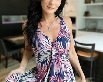 Puede incluir: Una mujer lleva un vestido maxi sin mangas con estampado de hojas tropicales en tonos azules, rosas y blancos. El vestido tiene un escote en V y un corpiño ajustado.