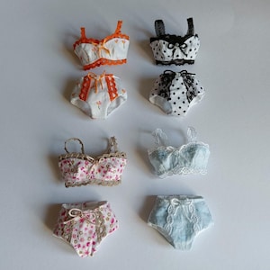 Può includere: Set di sei set di lingerie per bambole, tra cui due reggiseni e slip con motivi floreali, due reggiseni e slip a pois e due reggiseni e slip con bordino in pizzo.