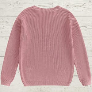 May include: A pink knitted sweater with long sleeves and a crew neck.