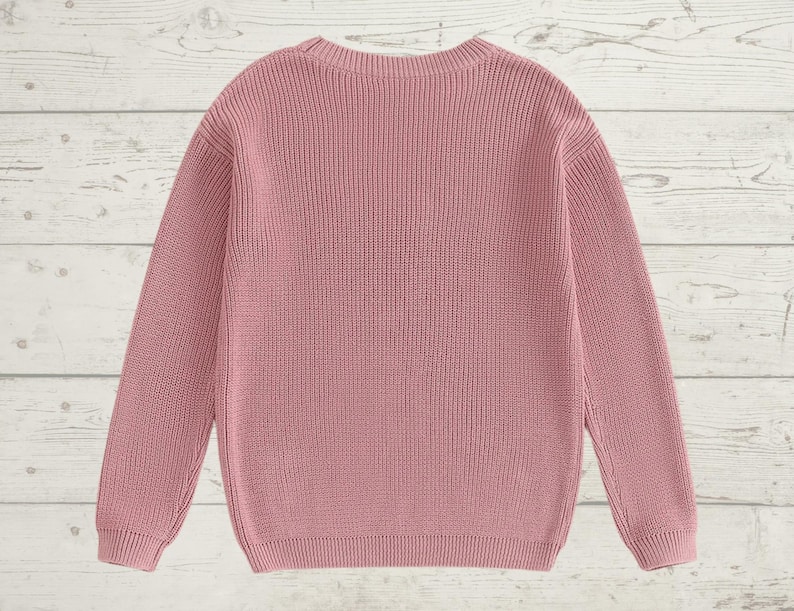 May include: A pink knitted sweater with long sleeves and a crew neck.