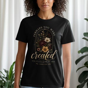May include: A black short-sleeve t-shirt featuring a central graphic of an arched floral arrangement with the text "PERHAPS YOU WERE created FOR SUCH A TIME AS THIS" and "Esther 4:14" in gold and white lettering with various colored flowers.