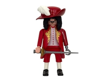 May include: A red and gold plastic figurine of a pirate wearing a red hat with a white feather, a red jacket, and holding a sword.