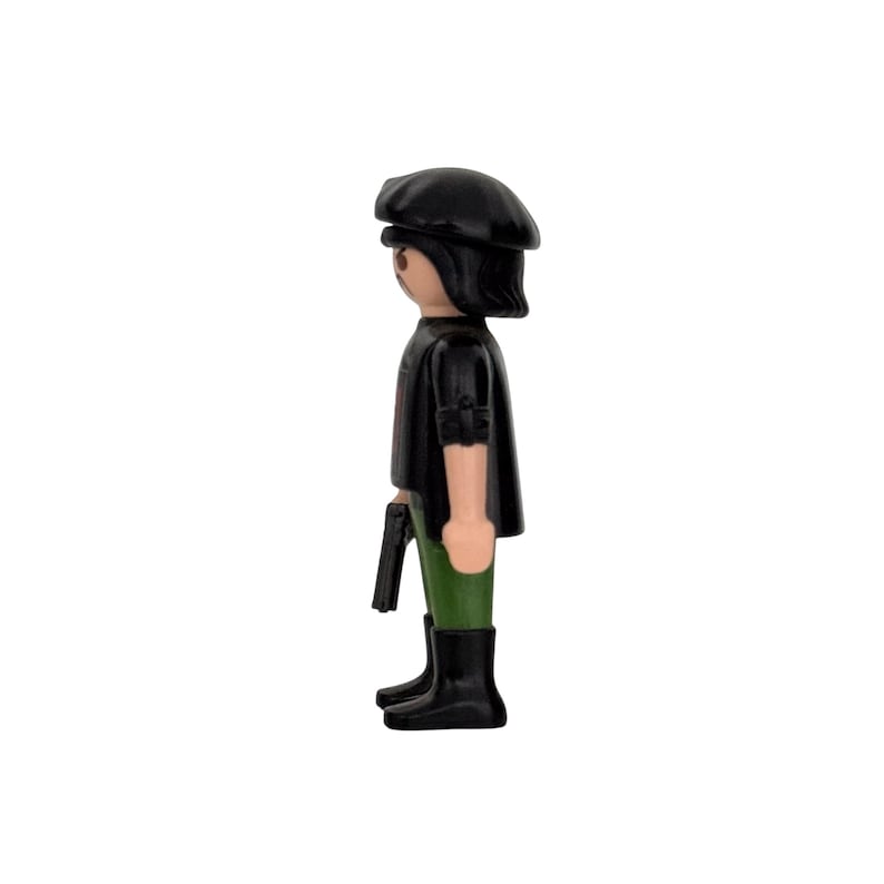 May include: A black and green plastic figurine of a person wearing a black beret, black jacket, and green pants. The figurine is holding a black gun in its right hand.