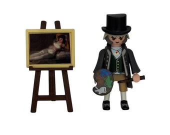 May include: A miniature figure of an artist holding a paint palette and a brush, standing in front of an easel with a painting of a reclining woman. The artist is wearing a black coat, a green vest, and a black top hat. The painting is framed in gold and has a yellow background.