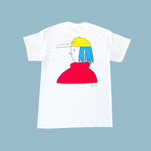 May include: White t-shirt featuring a cartoon illustration of a person wearing a red shirt, blue hair, and a yellow hat. The text "we were meant to be together" is printed above the illustration.
