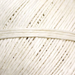 May include: Close-up of a ball of cream-coloured twine. The twine is tightly wound, with visible diagonal lines and a horizontal band. The texture appears rough and natural, suitable for crafts and packaging.