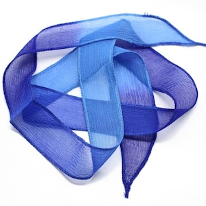 May include: A blue and light blue ombre ribbon with a satin finish. The ribbon is folded and twisted into a decorative shape.