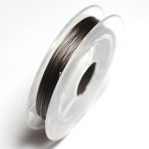 Puede incluir: Una bobina de alambre gris oscuro en una bobina de plástico transparente. El alambre está enrollado firmemente alrededor de la bobina, que tiene un pequeño agujero en el centro.