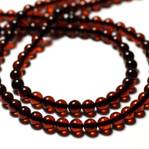 Può includere: Una collana di perle di ambra rosso scuro, infilate su un cordoncino e disposte in cerchio.