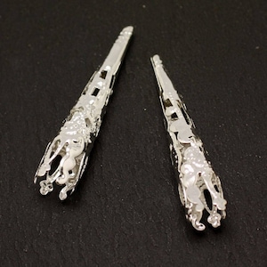 May include: Two silver metal cone-shaped bead caps with intricate floral designs.