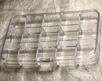 Op de afbeelding: Een transparante plastic opbergdoos met 12 vakken. De doos is leeg en heeft een scharnierend deksel.