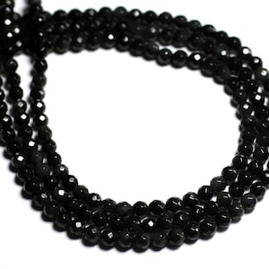 Könnte beinhalten: Eine Kette aus schwarzen Edelsteinperlen, wahrscheinlich Obsidian, mit facettiertem Finish. Die Perlen sind auf einem durchsichtigen Faden aufgefädelt und in einem Kreis angeordnet.