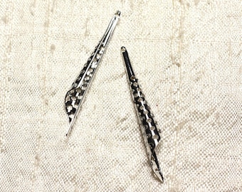 May include: Two silver metal decorative pieces shaped like a cone with a hole pattern. The pieces are on a white fabric background.