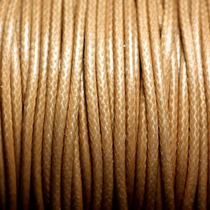 Peut inclure: Gros plan d'une bobine de cordon ciré beige. Le cordon est enroulé serré et a une finition lisse et polie.