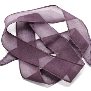 May include: A close-up of a purple ribbon with a textured surface. The ribbon is folded and twisted, creating a decorative design.