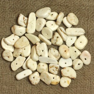 Può includere: Una collezione di perline di pietra naturale di colore bianco, bianco sporco e crema con fori praticati al centro. Le perline sono di varie forme e dimensioni, e alcune presentano delle macchie marroni.
