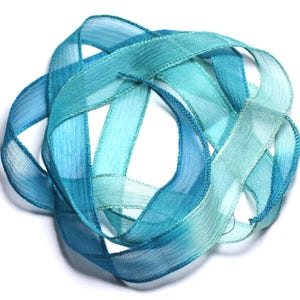May include: A bundle of teal blue and green ombre ribbon. The ribbon is made of a sheer, silky fabric and is tied in a knot.