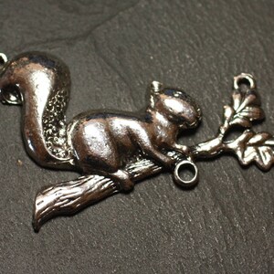 Puede incluir: Encanto de plata con una ardilla sentada en una rama con una hoja de roble. El encanto tiene dos anillos de salto para sujetarlo a joyas.