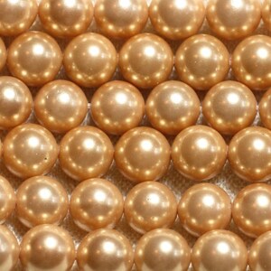 May include: A close-up of a strand of pearl-like beads. The beads are a light gold colour and have a smooth, shiny finish.