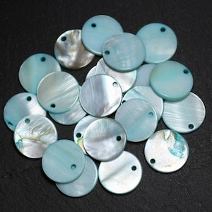 Könnte beinhalten: Eine Sammlung runder, hellblauer, irisierender Muschelscheiben mit einem kleinen Loch in der Mitte. Die Scheiben liegen auf einer schwarzen Oberfläche.