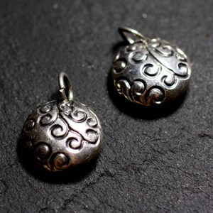 Peut inclure: Deux breloques en argent avec un motif en spirale. Les breloques sont rondes et ont une boucle en haut pour les attacher à un collier ou un bracelet.