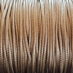 Puede incluir: Primer plano de un carrete de cordón encerado beige. El cordón está enrollado apretado y tiene una textura suave y sedosa.