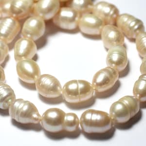 May include: A strand of off-white baroque pearls. The pearls are oval shaped and have a slightly iridescent sheen.