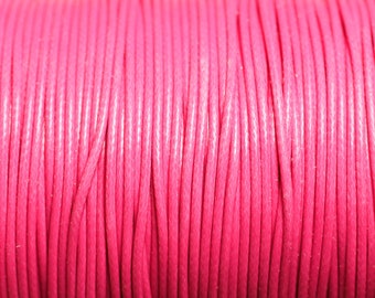 May include: Close-up of a spool of bright pink waxed cord. The cord is tightly wound and has a smooth, glossy finish.