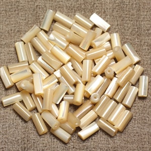 Peut inclure: Un tas de perles de coquillage blanches et beiges irisées de forme cylindrique.