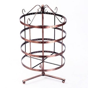 May include: A three-tiered rotating earring stand with a copper finish. The stand has a circular base with three legs and a decorative top.