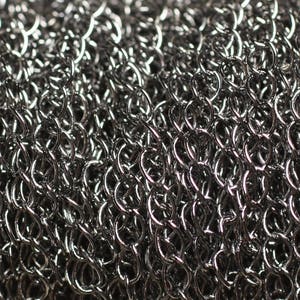 Peut inclure: Gros plan sur un maillage de cotte de mailles argentée, montrant le motif tissé complexe des anneaux métalliques.