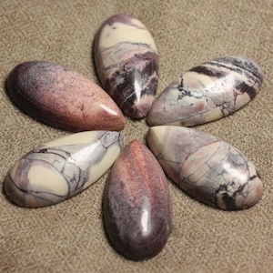 May include: Six smooth, oval-shaped stones with a swirling pattern of white, grey, and pink.