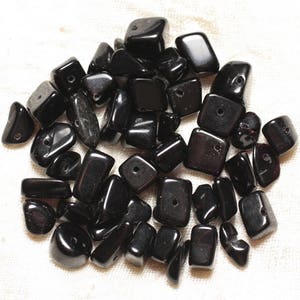 May include: A pile of black gemstone beads with holes drilled through them. The beads are various shapes and sizes, including square, rectangular, and oval.