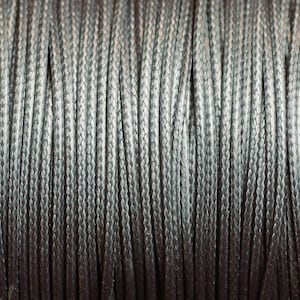 Puede incluir: Primer plano de un carrete de cordón gris plateado. El cordón está enrollado apretado y tiene un acabado liso y ligeramente brillante.