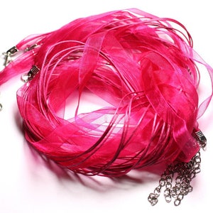 May include: A collection of bright pink organza ribbon necklaces with silver clasps and chain extensions. The sheer fabric is gathered and layered, creating a full, textured appearance. The ribbons are a vibrant fuchsia colour.