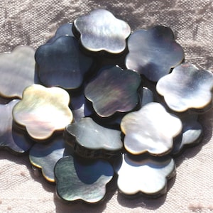 Puede incluir: Un grupo de 15 botones de madreperla negra iridiscente en forma de flor. Los botones tienen un diámetro de aproximadamente 2,5 cm y un diseño de flor de cinco pétalos.