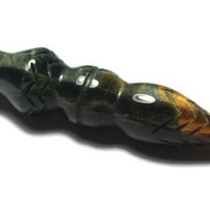 Może przedstawiać: Wisiorek z niebieskiego tygrysiego oka, rzeźbiony w kształcie grotu włóczni. Wisiorek ma otwór na górze do sznurka lub łańcuszka.