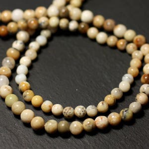 Puede incluir: Una hebra de cuentas de piedras preciosas de color crema, marrón y blanco. Las cuentas son redondas y tienen un aspecto natural y orgánico.