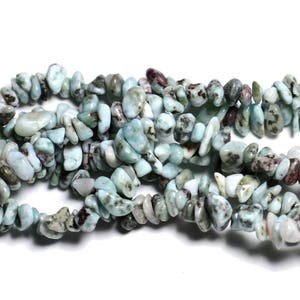 May include: Strands of polished, irregular-shaped gemstones in shades of pale blue, white, and brown. The beads are strung together, creating a textured and organic appearance. The gemstones are likely used for jewelry making.