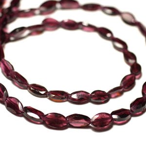May include: Two strands of oval, deep burgundy beads. The beads are strung together, resembling a necklace. The faceted surface of the beads catches the light. The background is plain white. The beads are approximately 0.8 cm in length.