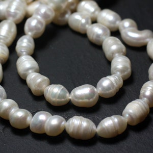 Pode incluir: Um fio de pérolas barrocas brancas, de forma irregular, enfiadas em um cordão branco. As pérolas estão dispostas em duas fileiras, criando um efeito em camadas.
