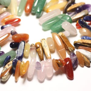 May include: A collection of colorful, polished gemstone chips in various shapes and sizes. The chips are arranged in a circle, with some overlapping. The colors include red, orange, yellow, green, blue, purple, and brown.