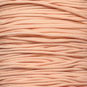 May include: Close-up of a reel of peach-coloured elastic cord. The cord is tightly wound and has a smooth, slightly shiny finish.