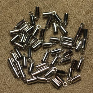 Op de afbeelding: Een stapel zilverkleurige metalen eindkappen voor koorden of sieraden maken. De doppen zijn cilindrisch met een kleine lus aan de bovenkant.