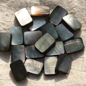 Könnte beinhalten: Eine Sammlung rechteckiger Muschelsteinchen in Schwarz und Irisierend. Die Steinchen sind glatt und haben ein natürliches, organisches Aussehen.