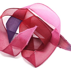 May include: A bundle of three sheer ribbon rolls in shades of pink, red, and purple. The ribbon is folded and twisted, creating a decorative display.